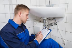 young,plumber,writing,on,clipboard,with,pen,in,kitchen,room